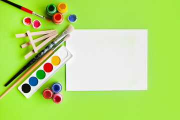 various painting supplies and blank white canvas on a green background. flat lay. top view. copy space. back to school.