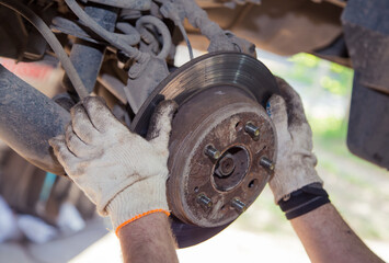 The man's hands remove the worn brake disc from the rear wheel hub. In the garage, a person changes the failed parts on the vehicle. Small business concept, car repair and maintenance service.