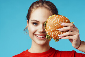 cheerful woman in red t-shirt hamburger in hands fast food blue background