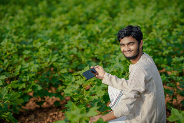 Indian farmer using smart phone at green cotton crop