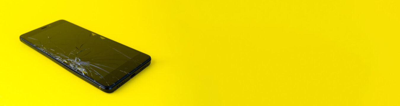 A mobile phone with a broken screen lies on a yellow background. A broken smartphone. Electronic gadget in need of repair. banner for placement on the site