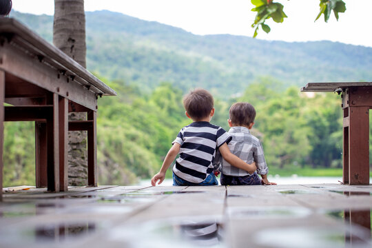 Asian brother talks to comfort his brother by the lake.