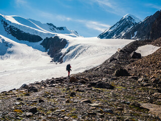 Solo trekking in the mountains. A male hikers down the mountain path. In the background, large snow-capped mountains.