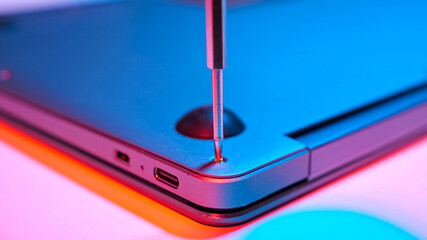 Close-up of screwing bolt into laptop cover in red blue light.