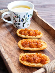 Cardamom rusks with cloudberry jam and cup of green tea on a wooden tray