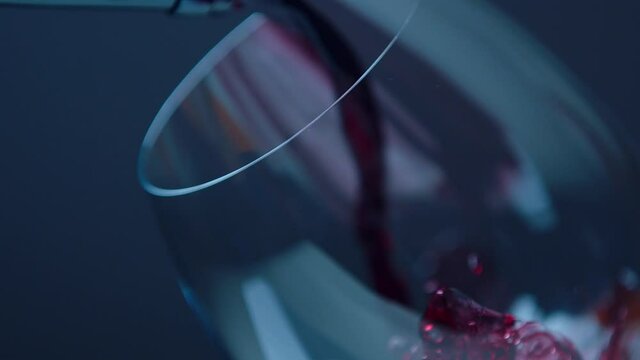 Slow motion of pouring red wine from bottle into glass or goblet on dark background . Close up of red wine forms beautiful wave in glass. Beautiful stock footage for wine commercial . 