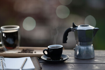 Closed up with a hot coffee, moka pot and note papers place on the wooden table with bokeh background.
