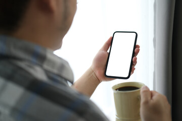 Closed up with a man who using modern smartphone and holding a cup of coffee, blank screen of smartphone.