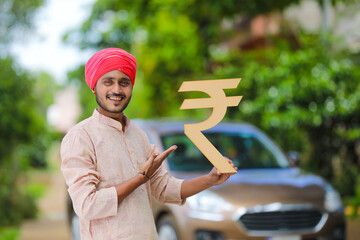 Indian farmer standing with his car and showing rupees symbol