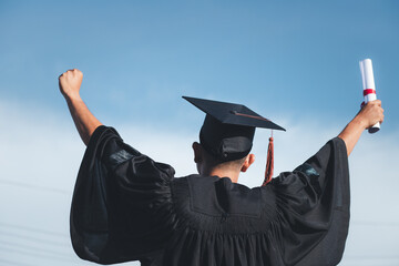 graduation idea A graduate holds up a certificate on a sky background.
