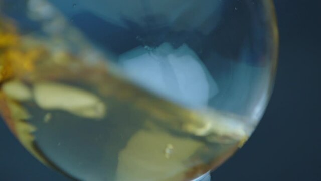 Waving gold white wine in a glass on defocused dark background . Beautiful stock footage for wine commercial . Close up video of wine mixing process inside goblet . Shot on ARRI ALEXA in Slow Motion .