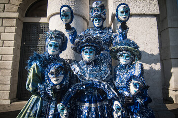 Group of males and females in masks and blue carnival costumes standing in front of an old building