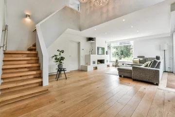 Deurstickers Cozy house interior with a wooden floor, large gray sofa, and stairs leading to the second floor © Casa Media/Wirestock