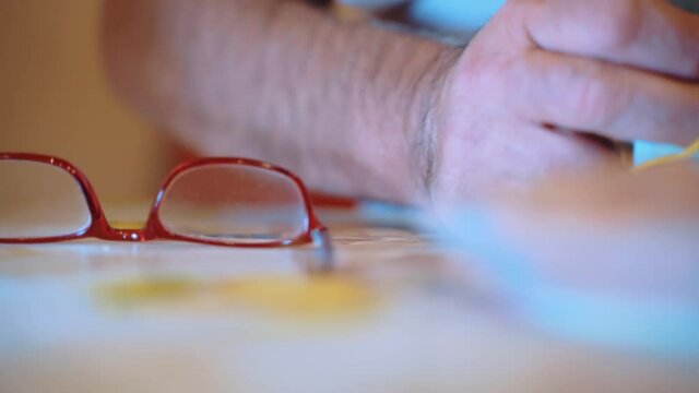 Senior man sitting at the table with eyeglasses and tying up the pack of euro paper currency with an elastic band, old man making his budget and saving money for further investments in business or