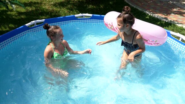 Happy girls swim in outdoor leisure pool on sunny summer day, swimming