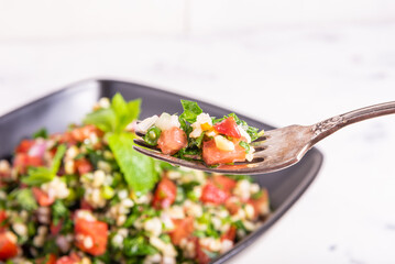Fork with tabbouleh salad on the background of a bowl of salad