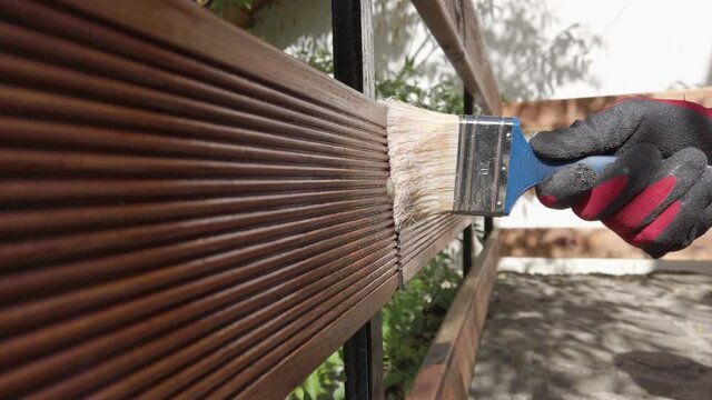 Hand in glove painting fence of impregnated ship floor planks. Carpenter applying protective layer of varnish.