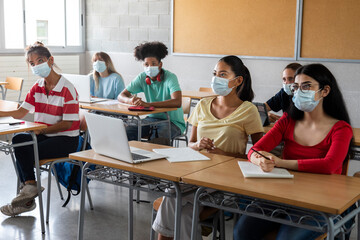 Group of multiracial teen highschool students wearing face mask listen to teacher lesson.