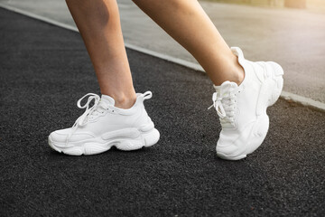 close-up of female legs of a Caucasian girl shod in white women's sneakers in a park against the background of a treadmill