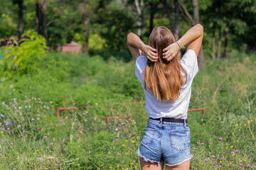  young shapely girl, with long hair, dressed in a T-shirt and shorts, stands with her back, on a...