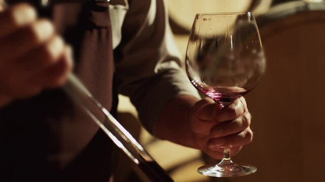 Winemaker checking on wine by sampling pipette . Man testing wine in a factory or warehouse . Portrait of a senior well-dressed winemaker checking the wine . Shot on ARRI ALEXA Camera Slow Motion .
