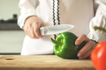Cutting vegetables, green sweet pepper on a wooden board with knife in chef in modern kitchen