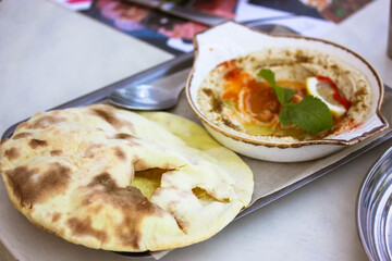 Appetizer classic hummus with olive oil, paprika, lemon, spices, green mint leaf in white ceramic bowl. Pita bread on a metal tray. Chickpea, vegetarian, vegan dish. Arabic food, tasty snack top view.
