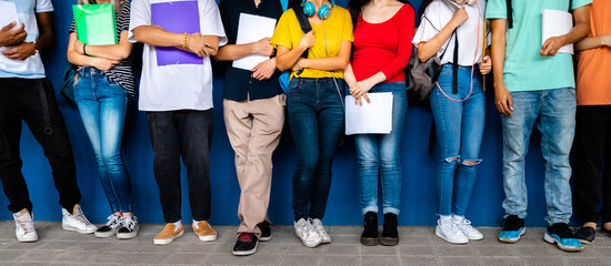 Horizontal banner image of group of multiracial teenage high school students ready to go back to school standing against blue background wall.