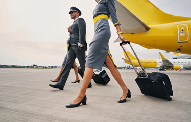 Elegant aviator and two stylish stewardesses with luggage moving ahead