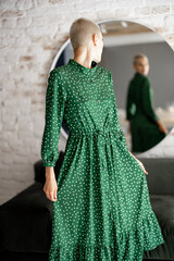 Stylish woman in green dress looks at herselfes in the mirror, getting ready to go out. Female...