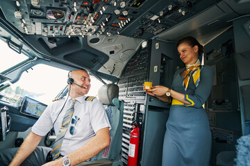Joyous male pilot being served a beverage in the cockpit - obrazy, fototapety, plakaty