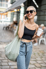 Stylish and trendy woman walks with a coffee and bag outdoors. Street fashion and lifestyle concept