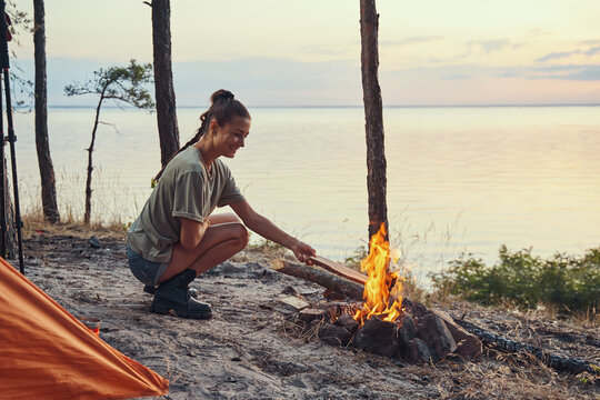 Female hiker throwing log into campfire outdoor