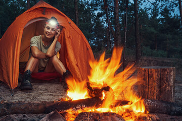 Female Caucasian camper inside tent watching bonfire - Powered by Adobe