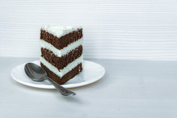 A teaspoon and a slice of buttercream chocolate sponge cake is located on the left.