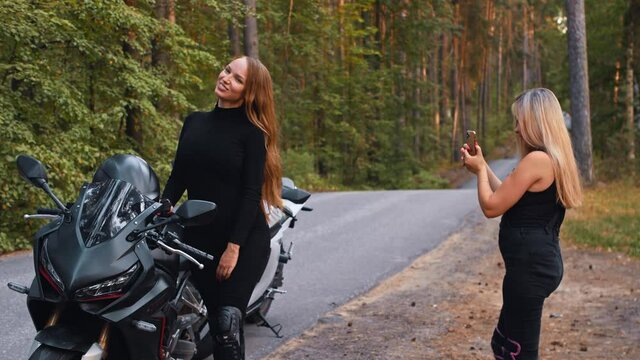 Smiling women friends taking photos on motorbikes in the forest