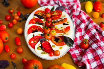 Italian caprese salad with mozzarella cheese and tomatoes garnished with cherry tomatoes, pesto sauce, balsamic vinegar and basil leaves 
