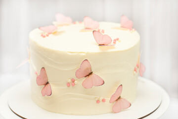 Birthday cake for a girl decorated with white cream with pink butterflies on the background of a home interior.