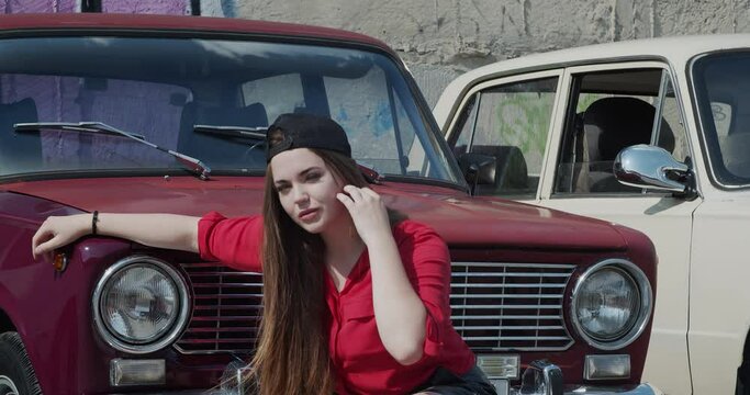 A young woman poses against the background of an old car
