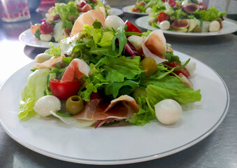 light diet salad made from a mix of greens, cherry tomatoes, mozzarella cheese and prosciutto slices
