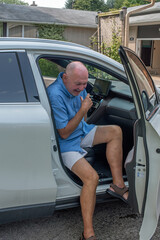 A older gay man wearing shorts, gets out of the passenger seat of a car.
