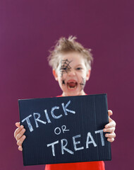 Happy cute kid with Halloween makeup, holding a blackboard with the text: Trick or Treat.
