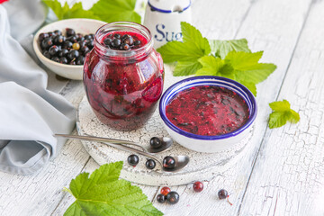 Jar of homemade fresh not boiled currant jam with shugar. Fresh berries black currant on white wooden background.