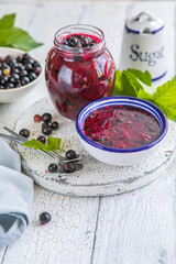 Jar of homemade fresh not boiled currant jam with shugar. Fresh berries black currant on white wooden background.
