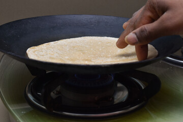 Making roti (Indian Chapati) on roti tawa made of wheat with hand on gas stove