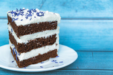A slice of chocolate sponge cake with a layer of butter cream located on the left. Purple sprinkles. Blue background.