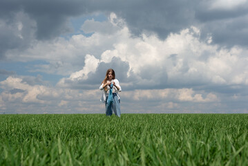 little teenager girl running in a field of green grass, against the backdrop of a cloudy sky