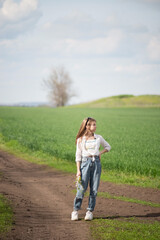 fashionable little girl in a field on a path, against a background of clouds