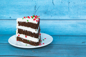 A piece of chocolate sponge cake with a layer of butter cream located on the left. Blue background. Red-green dusting