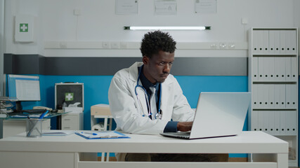 Portrait of doctor in medical cabinet sitting in uniform at desk. Close up of medic working and typing on modern laptop for professionals, healthcare private hospital office